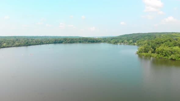 slow rotating drone flight over a lake in a forest with people kayaking under a blue summer sky with