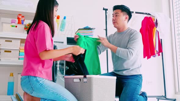 Husband helping wife putting clothes in washing machine.