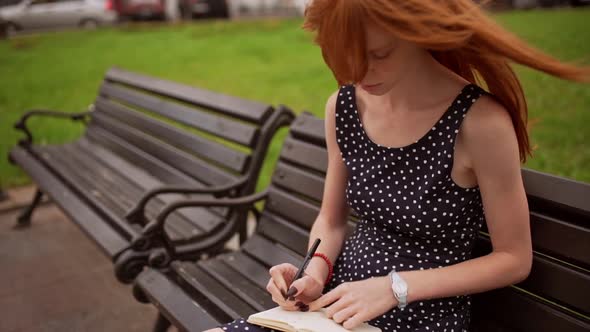 Ginger Teenage Caucasian Girl in Black Polka Dot Dress Writing Notes with Hair on Her Face
