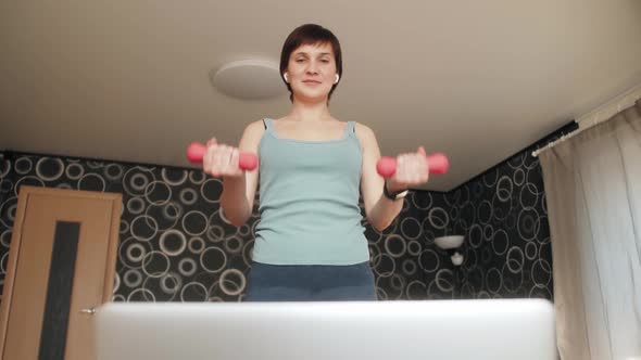 Woman in activewear doing fitness exercises pumping muscles with dumbbells with help of instructor.