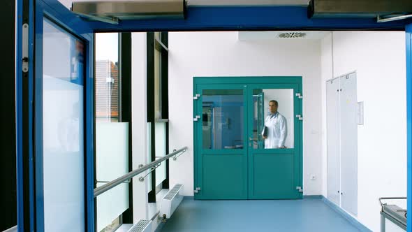 Male doctor holding a clipboard and walking in passageway of hospital