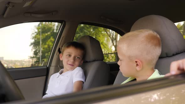 Two Cute Little Boys are Sitting at the Wheel of Their Father's Car and Talking