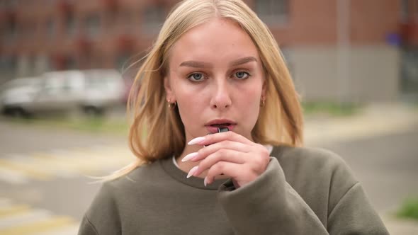 Close-up of a smoking woman in the city. Young woman sadly inhales smoke
