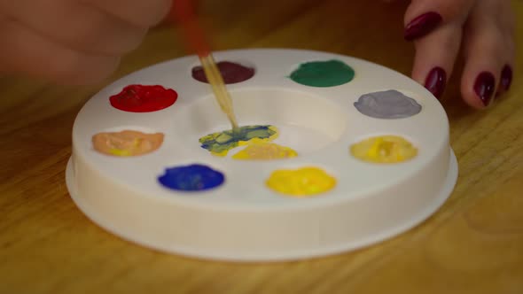 The Artist Mixes Yellow and Blue Paint on a Palette with a Paintbrush.