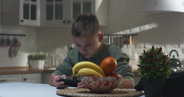 Boy Playing on His Smartphone in the Kitchen