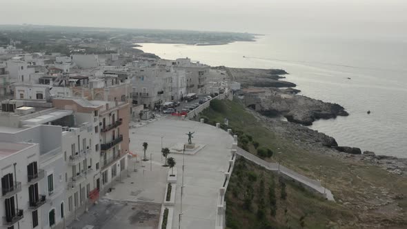 Aerial circle view with descending orbit on the coast with statue of Domenico Modugno. Polignano a M