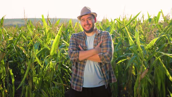 Self Confident Young Man Farmer Stands Arms Crossed in a Cornfield Front View Looking at the Camera