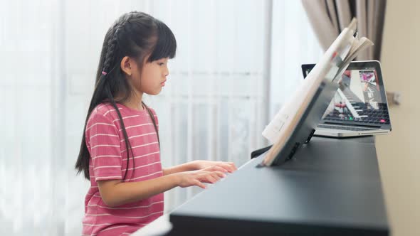 Homeschool Asian little young kid girl learning piano by watch music online instruction from tablet