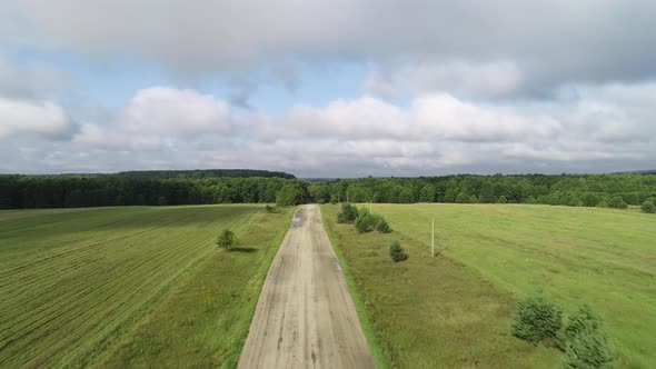 Slow Rise To a Height Above a Dirt Rural Road Running Through Green Fields.