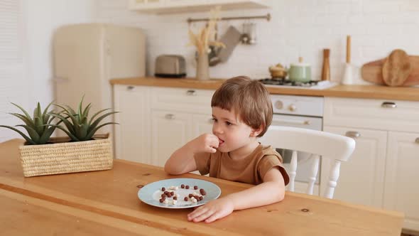 a Little Caucasian Boy Eats Krunchy Breakfast and Enjoys It at Kitchen Table