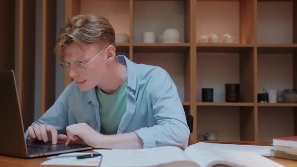 Young Man Actively Typing on the Laptop Working From Home