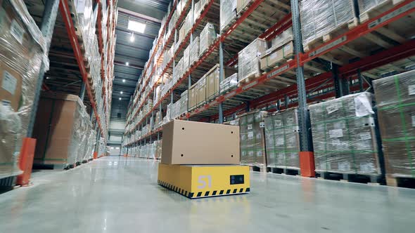 Industrial Robot is Riding Along the Storehouse with a Box