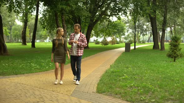 Adult Dad Walking With Loving Teen Daughter in Park, Sharing His Life Experience