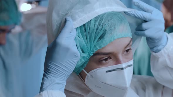 Female Doctor Putting on a Medical Cap, Protective Mask KN95, Glasses and Hazmat