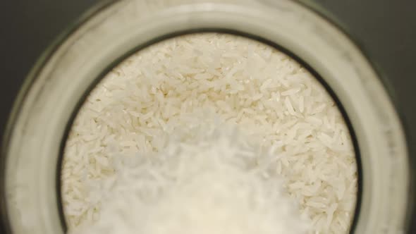 White Rice Grains Pouring Into A Glass Jar - Slow Motion