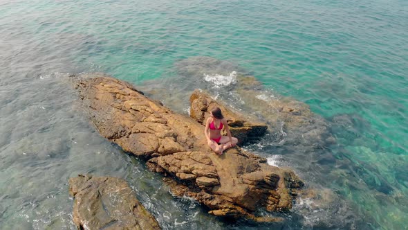 Girl in Red Bikini Sits on Huge Stone in Sea Waving Hand