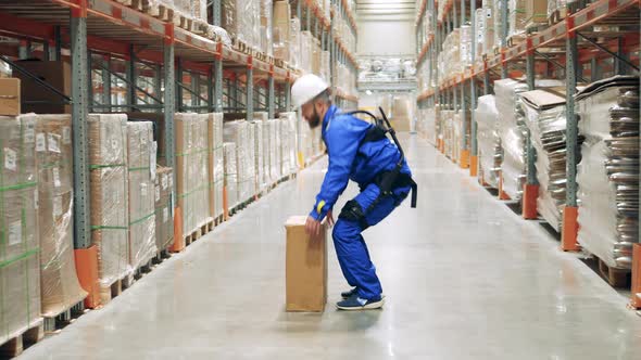 Storage Worker is Lifting a Box While Wearing Ergoskeleton