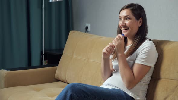 Happy Woman Holding Pregnancy Test in Hands Sitting on Sofa
