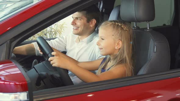 A Little Girl Is Sitting with Her Dad in the Car and Pretending To Turn the Steering Wheel