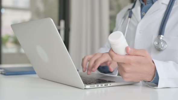 Close Up of Doctor Searching on Laptop While Holding Medicine