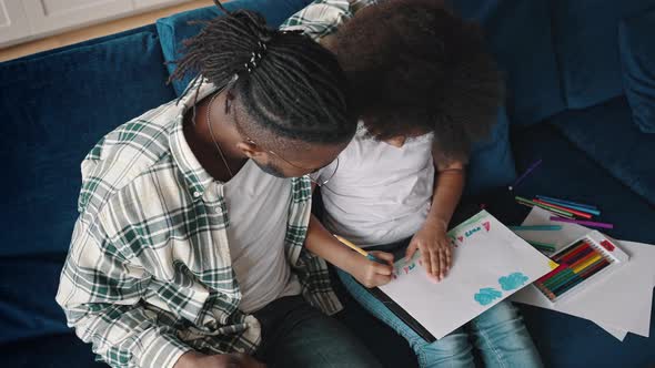 Top View on Little African American Girl Drawing Marine Picture Sitting on Sofa with Her Father