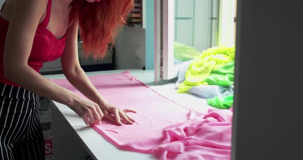 Female Dressmaker Measuring a Pink Silk with Ruler on Surface in Atelier