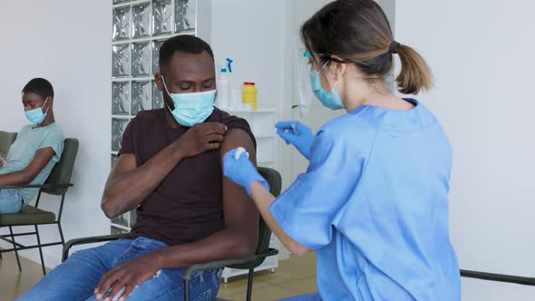 Female doctor vaccinating young black male patient