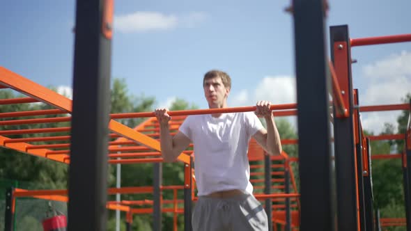 Confident Young Sportsman Doing Pullups on Gymnastic Bar Outdoors in Sunshine