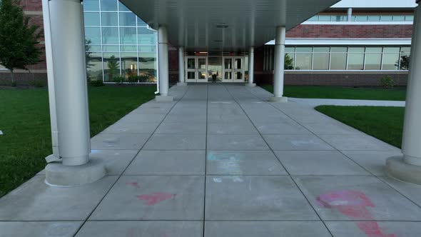 Low aerial approach towards school entrance. Sidewalk chalk drawings on concrete from elementary sch