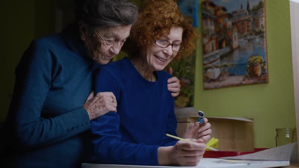 Senior Couple 90 Years Old Mom and Older Daughter Hug and Painting