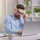 Tired of working at a laptop, a business man takes off his glasses while sitting at a work desk. - VideoHive Item for Sale