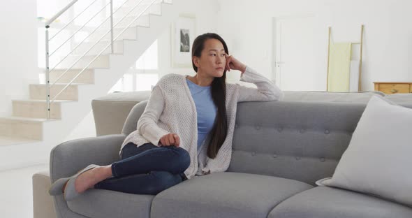 Thoughtful asian woman sitting at sofa at home
