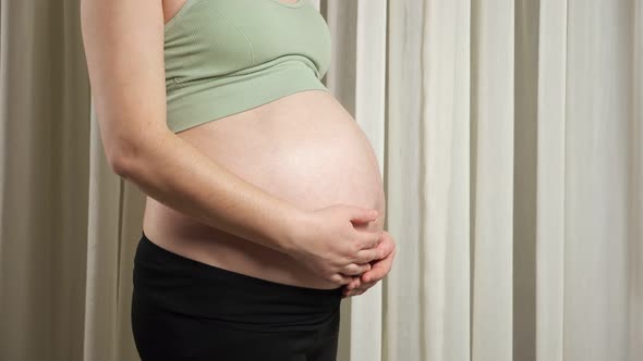 Young Woman in Sportswear Touches Pregnant Belly Caressing