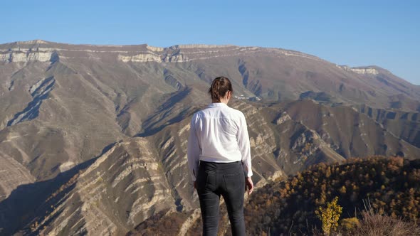 Young Woman Walks and Raises Hands Against Mountains