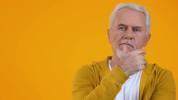 Thoughtful Male Pensioner on Orange Background, Choice Hesitation, Problem