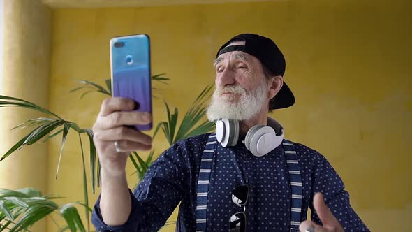 Modern Senior Man with Gray Beard in Trendy Cap Looking in Phone Camera