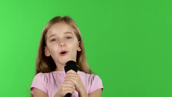 Child Girl Sings the Song Into the Microphone. Green Screen