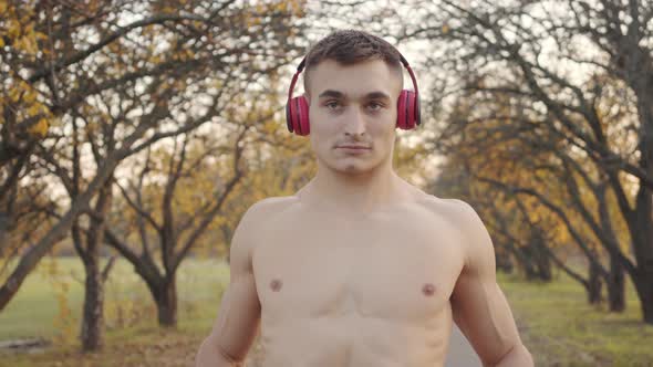 Adult Caucasian Sportsmen with Naked Torso Warming Up in the Autumn Park, Strong Boy in Headphones