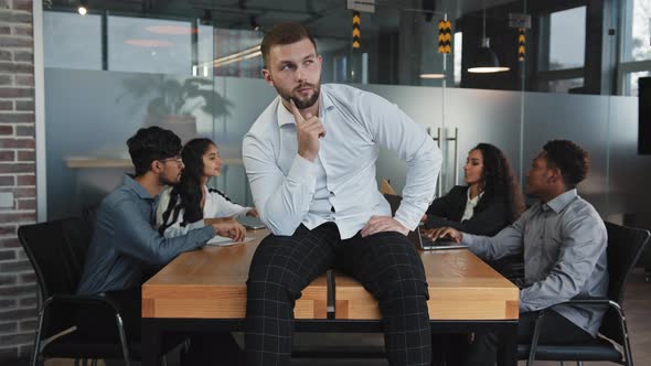 Thoughtful Young Guy Looking Away Sitting on Table in Office Serious Man Thinks About Solving