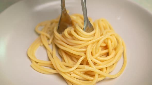 Close-up shot of hand holding a tong picking up cooked spaghetti placing on a plate.