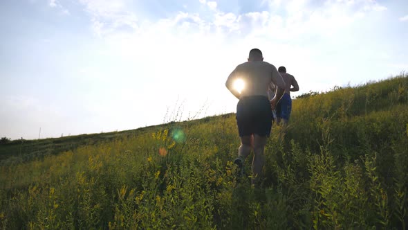 Group of Young Men Running Up the Green Hill Over Blue Sky with Sun Flare at Background. Male