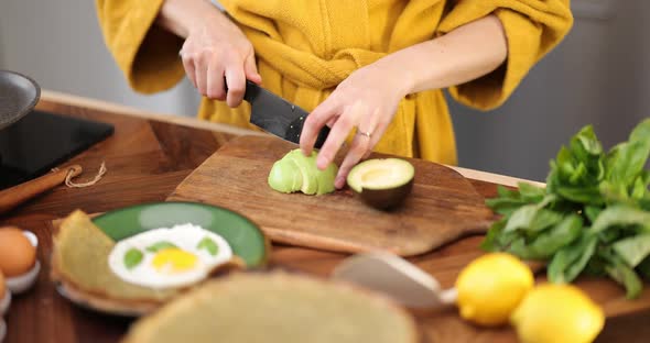 Woman Prepares Breakfast with Eggs and Avocado