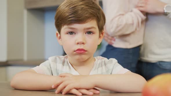 Child sitting at a table and parents dancing behind him