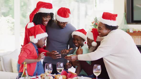 African american family in santa hats using smartphone while standing near dining table after having