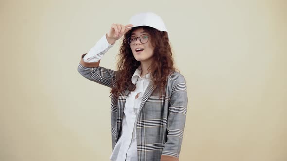 The Young Woman with Curly Hair Wears a White Engineer's Helmet Looks Around and Smiles