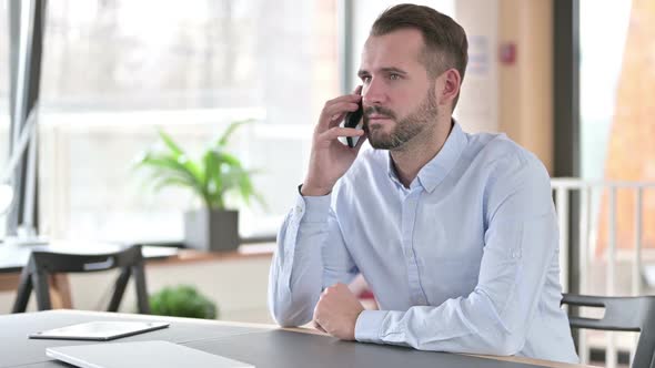 Serious Young Man Talking on Smartphone in Office