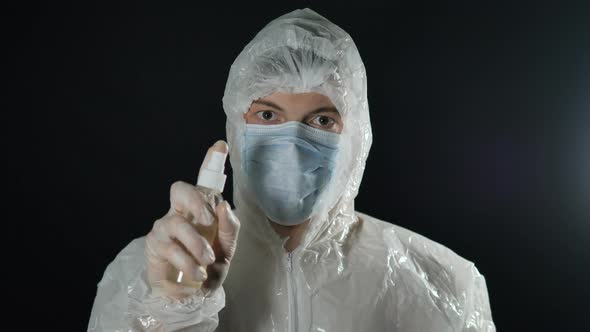 Portrait of a Doctor Man in a Medical Mask and Protective Suit Sprays an Antiseptic Spray