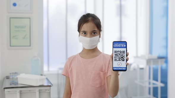 Little Girl in Medical Mask Showing Smartphone in Her Hand with Mobile Application for Vaccination