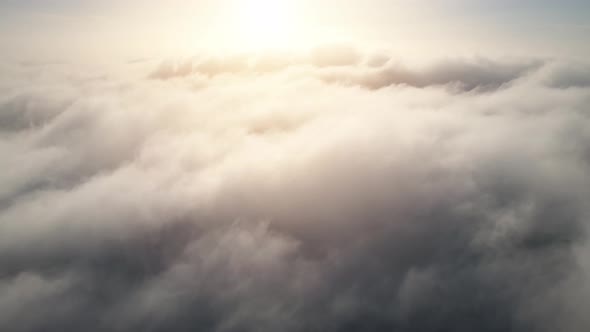 Aerial shot of flying over a layer of soft clouds at dawn