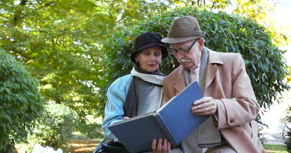 Portrait of Elderly Couple Relaxing on a Park Bench and Looking at a Photo Album
